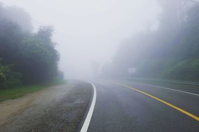 Empty road amidst trees against sky