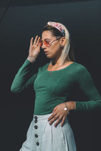 Young woman wearing sunglasses standing against black background