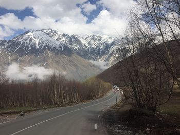 Road amidst trees and snowcapped mountains against sky