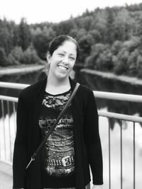 Portrait of smiling young woman standing against railing