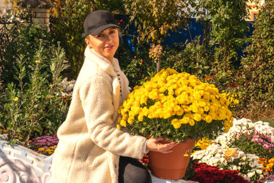 Portrait of a woman on an autumn sunny day, she is holding yellow chrysanthemums.