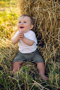 Gay boy kid blonde in white tank top sitting on a field of hay next to the stack during sunset