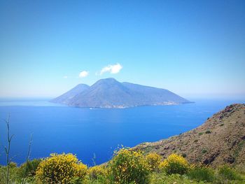 Scenic view of sea by mountains against blue sky