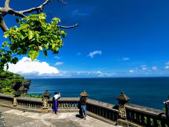 People standing by sea against blue sky