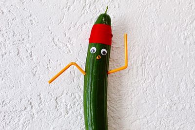 Close-up of cucumber with drinking straw and googly eyes on wall
