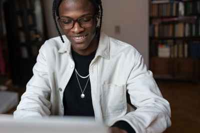 Smiling happy young african man in glasses using laptop at home, spending leisure time on internet