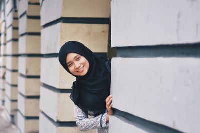 Portrait of smiling young woman standing by wall