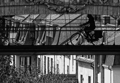 Silhouette of woman on bicycle on underbridge against buildings in black and white