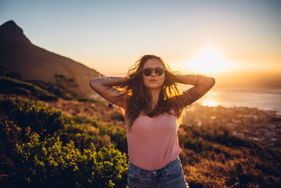 Beautiful young woman standing on land against sky during sunset