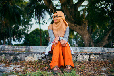 A portrait of a muslim woman smiling and sitting on a bench at park with flare