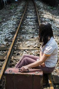 High angle view of woman with suitcase sitting on railroad track
