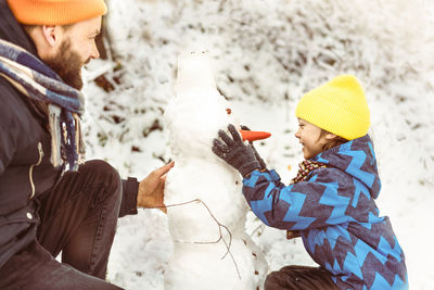 Joyful dad and son enjoying building a snowman.