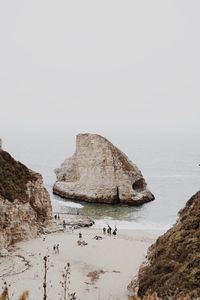 People on cliff by sea against clear sky
