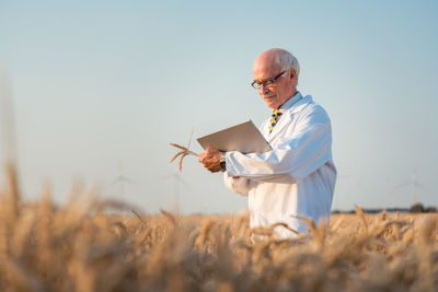 Scientist using digital tablet on field against sky