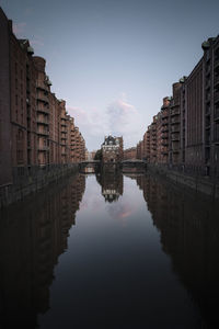 Canal amidst buildings in city against sky