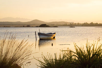 Boat moored in lake against sky during sunset