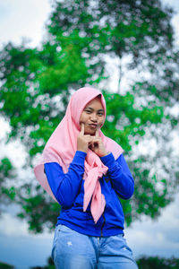 Portrait of young woman wearing hijab while standing against tree