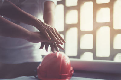Colleagues stacking hands by red hardhat on desk