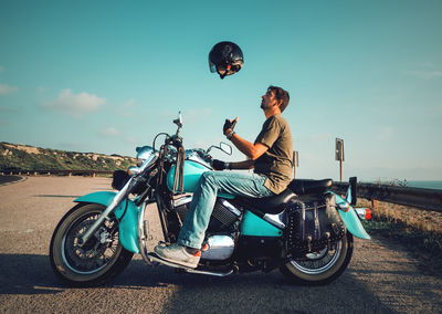 Side view of man riding motorcycle on road against sky
