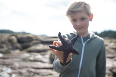 Portrait of boy holding camera against sky
