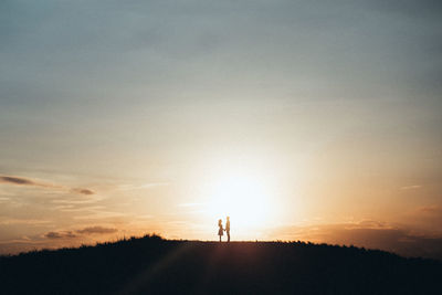 Silhouette people standing on landscape at sunset