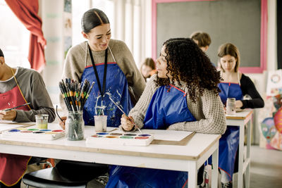 Smiling female teacher assisting teenage student during art class at high school
