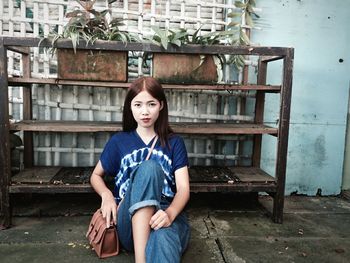 Portrait of young woman sitting against shelves with potted plants