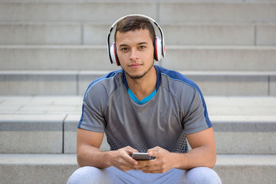 Young man using mobile phone while sitting on wall