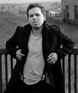 Portrait of young man standing against railing