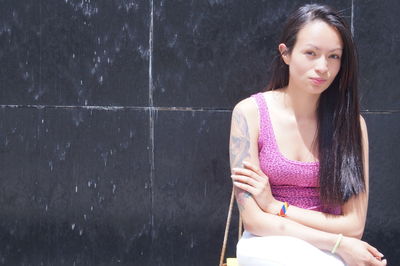 Portrait of young woman with long hair against wall