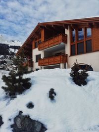 Snow covered house by building against sky