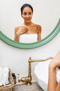 Reflection of woman applying cream on body in mirror at home