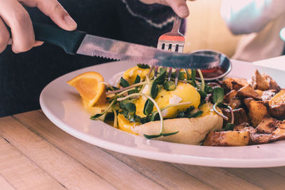 Cropped hands of person cutting eggs benedict