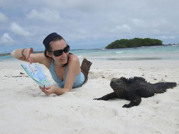 Smiling woman pointing at map to iguana on sand