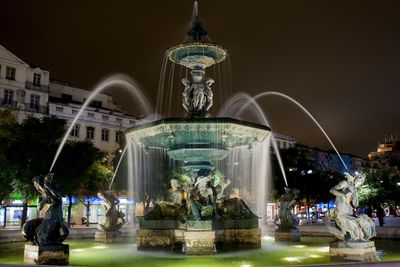 Fountain in front of building against sky at night