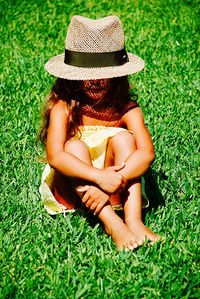 Full length of girl wearing hat sitting on grassy field