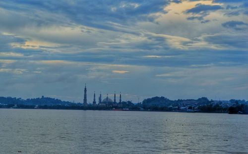 View of buildings by sea against cloudy sky