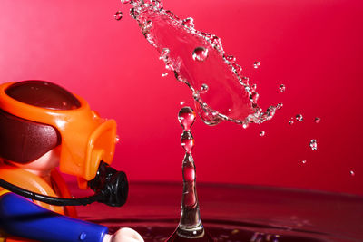 Close-up of toy diver by water against red background