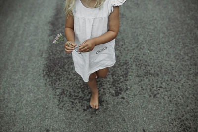 Low section of girl holding flowers on country road