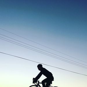 Silhouette man cycling against clear sky