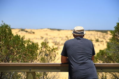 Rear view of man standing by railing against sky