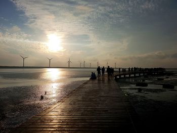 Silhouette people on pier at beach against sky during sunset