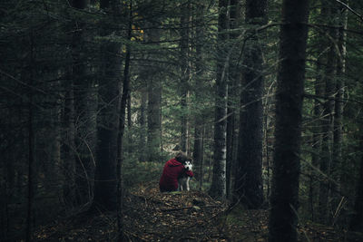 Rear view of woman embracing dog while sitting in forest