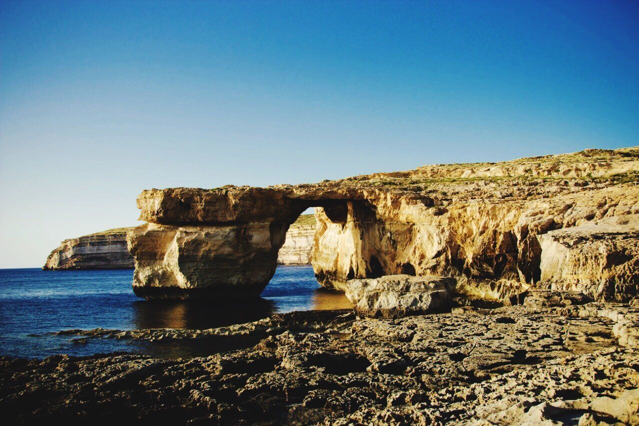 ROCK FORMATIONS BY SEA AGAINST CLEAR SKY