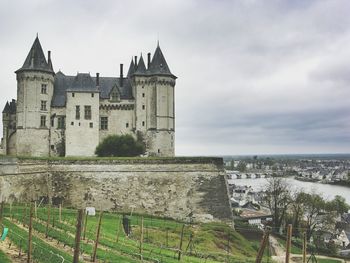 Chateau de saumur by river against cloudy sky