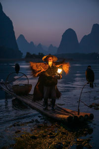 Portrait of man wearing hat standing on raft against mountain and sky