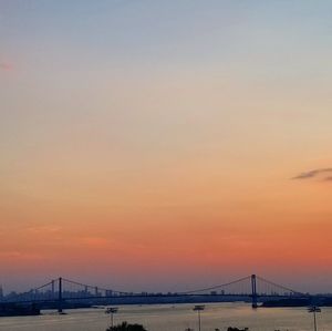 Suspension bridge over sea against sky during sunset