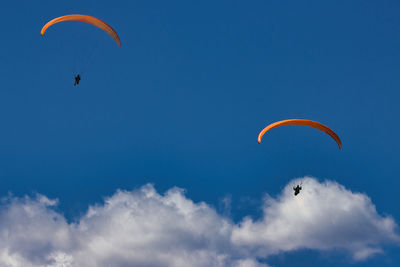 Low angle view of people paragliding against sky