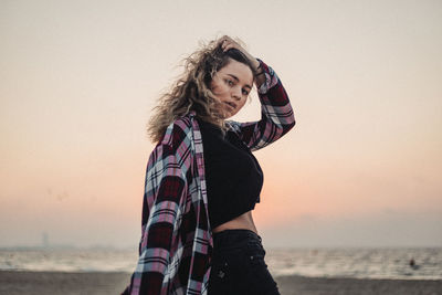 Portrait of beautiful young woman standing at beach against sky