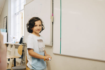 Smiling boy standing by whiteboard at classroom